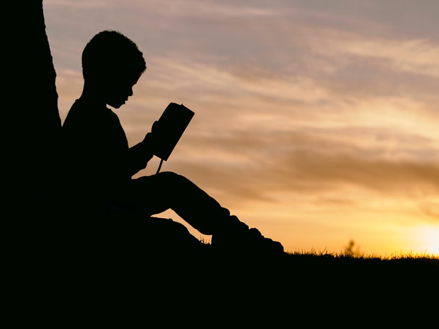 Silhouette of boy reading against sunset