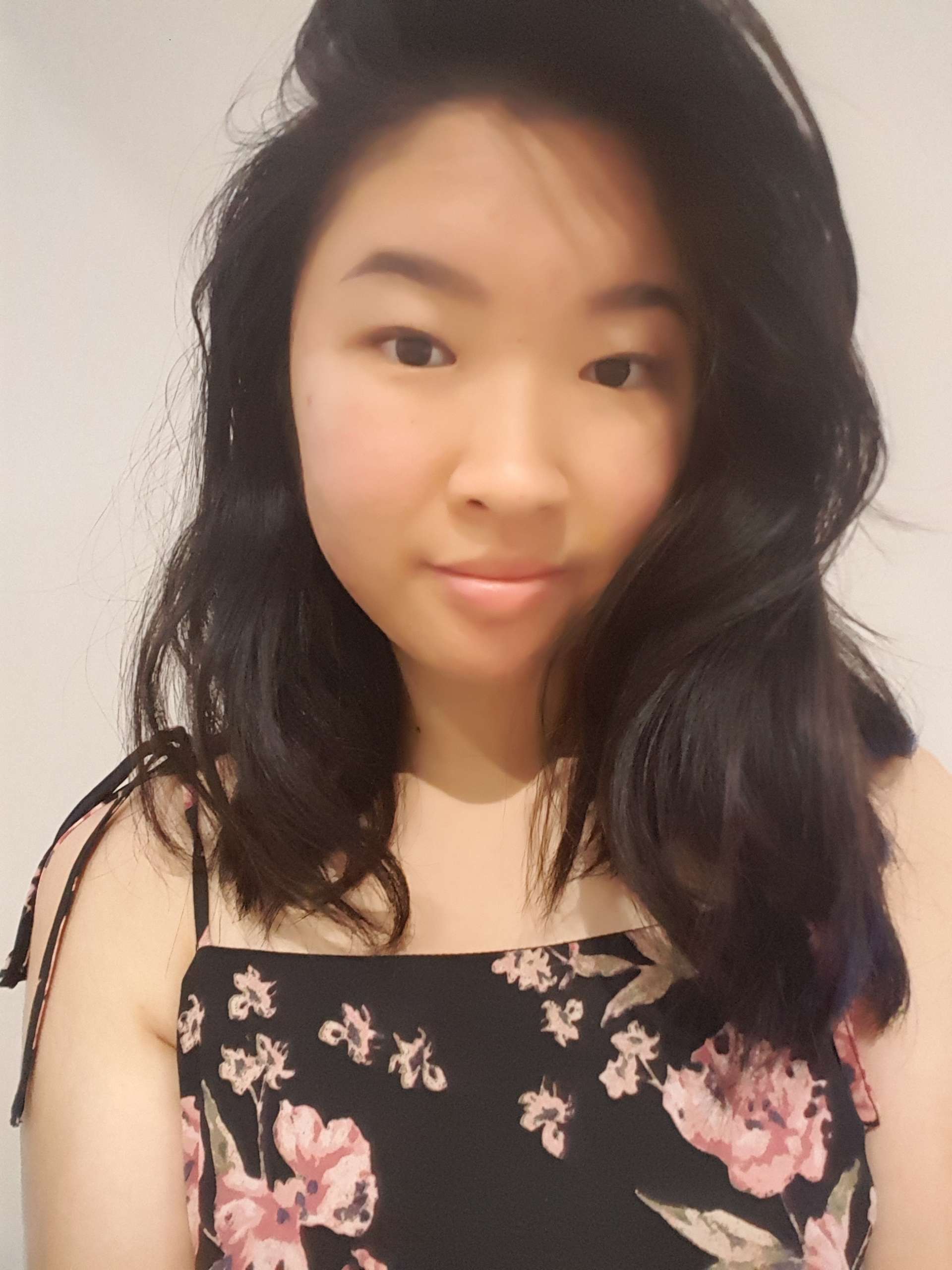 Writer, Christy Tan, weaing a black top with pink and green flowers. They are facing front on with long dark wavy hair parted on the right hand side.