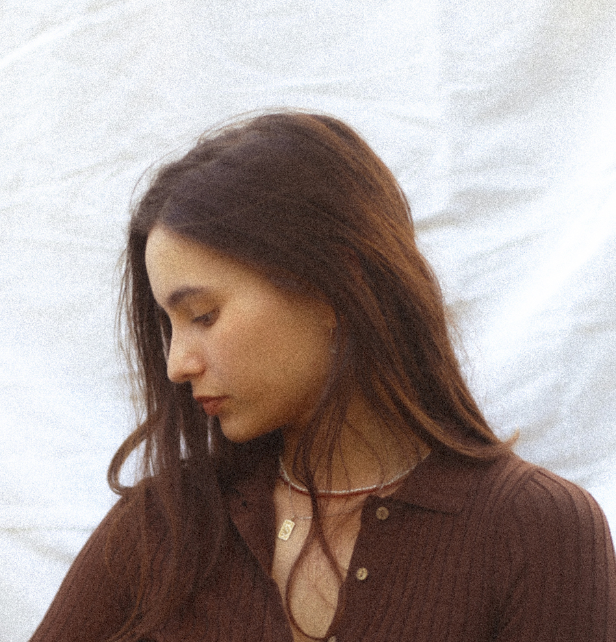 Writer, Kasumi Borczyk wearing a brown top, looking down at their right shoulder. They have long brown hair draped over their shoulders and the sunlight hits their hair from the right-hand side.